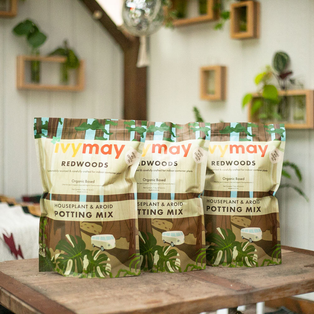 Three bags of IvyMay Redwoods Houseplant & Aroid Peat-Free Potting Mix on a wooden table inside of the IvyMay Hideaway.